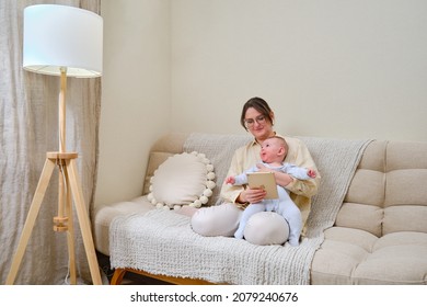 Happy woman mother with infant baby watching in a digital tablet iPad Apple while sitting on the home sofa in the living room - Moscow, Russia, November 01, 2021