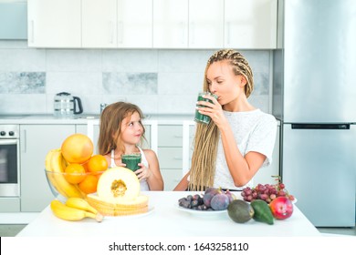 Happy woman mother and little girl daughter drinks green smoothie in kitchen. Mother and daughter with glass of natural detox smoothie in kitchen. Food supplements - Powered by Shutterstock