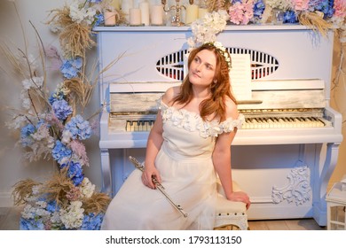 Happy woman musician sits with a flute in her hands on the background of an old piano