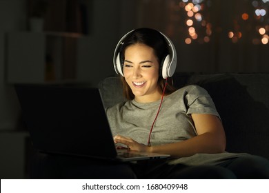 Happy woman in the night watching media on laptop sitting on a sofa in the living room at home - Shutterstock ID 1680409948