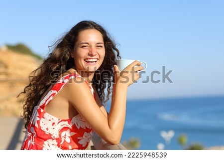 Happy woman on the beach drinking coffee laughing loud on asummer vacation
