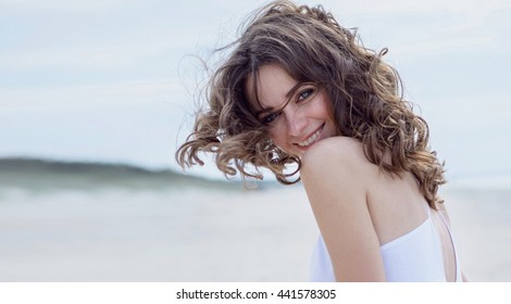 Happy woman on the beach. Portrait of the beautiful girl close-up, the wind fluttering hair. Spring portrait on the beach. Young pretty girl. Young smiling woman outdoors portrait. Close. ocean
