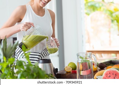 Happy woman on detox diet, pouring green cocktail from mixer into glass in kitchen - Powered by Shutterstock