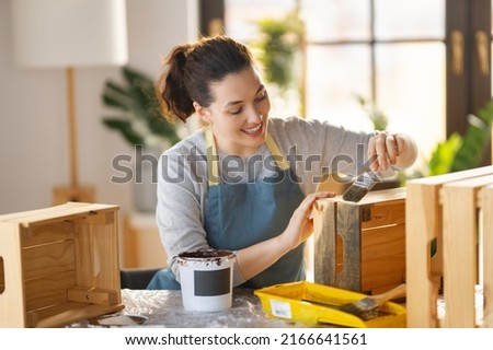 Happy woman is painting a wooden crate. Artisan is putting a protective coating on the garden box.
