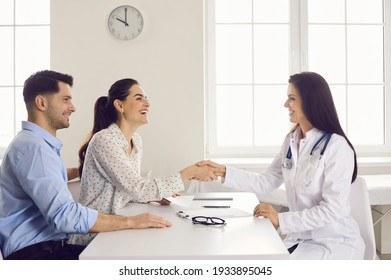 Happy Woman Patient Giving Gratitude Handshake To Doctor Get Good News About Pregnancy On Appointment At Clinic Office. Satisfied Caucasian Family Couple Visit Physician For Healthcare Consultation