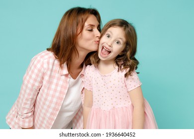 Una mujer feliz con ropa rosa se divierte con una linda niña de 5 a 6 años. Mamá hija pequeña se besa en la mejilla aislada en un estudio de fondo azul pastel. El concepto de la familia del amor por el Día de la Madre Foto de stock