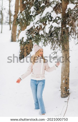 Happy woman in a pink coat and hat walks in the winter park.
The concept of the holiday, Christmas