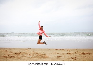 Happy woman with pink coat jump up over beachside, summer vacation concept