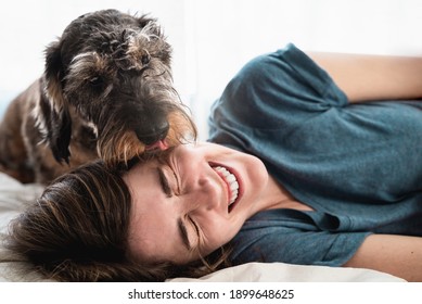 Happy Woman Playing With Her Dog Inside Home During Lockdown Isolation - Pet Licking Owner Face - Focus On Face