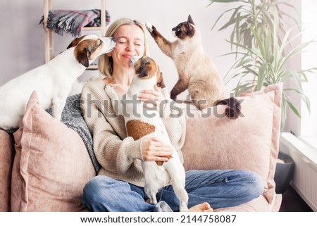 Happy woman playing with her dog on the couch at home. Dog licking middle aged woman in the living room