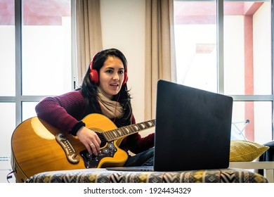 Happy Woman Playing Her Guitar While Following Tutorial In Her Laptop.