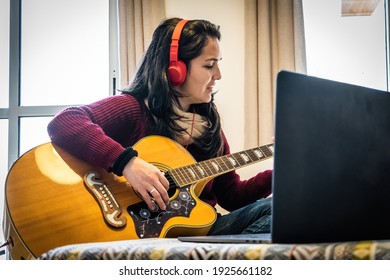 Happy Woman Playing Her Guitar While Following Tutorial In Her Laptop.