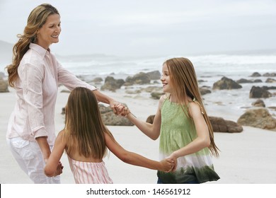 Happy Woman Playing Ring Around The Rosy With Daughters On Beach