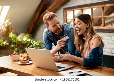 Happy woman pointing on something on laptop screen while shopping on the internet with her husband at home. - Shutterstock ID 1936178101