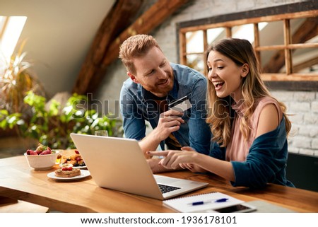 Happy woman pointing on something on laptop screen while shopping on the internet with her husband at home.