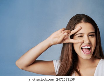 Happy woman, portrait and face with peace sign for friendly, funky or positive attitude on a blue studio background. Female person, brunette or young model with smile or emoji for cool, fun or humor - Powered by Shutterstock