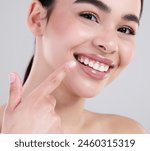 Happy woman, portrait and pointing with teeth for dental care, hygiene or treatment on a gray studio background. Closeup of young female person with big smile for tooth whitening, lip gloss or glow