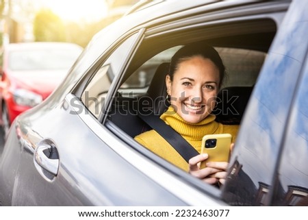 Happy woman portrait sitting on the back seat of a taxi car in the city looking out of the window - Smiling young caucasian woman using phone and car service - Travel and commuting concepts