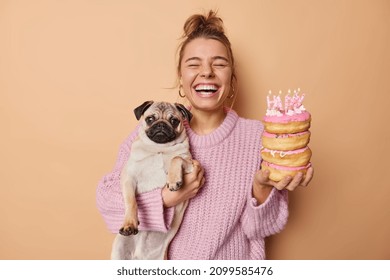 Happy woman poses with adorable oug dog and donuts going to blow candles celebrates pets birthday enjoys magic time wears knitted sweater isolated over beige background. Two best friends entertain - Powered by Shutterstock