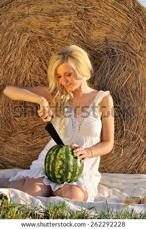 Happy woman posing with watermelon wearing white dress and hay as background