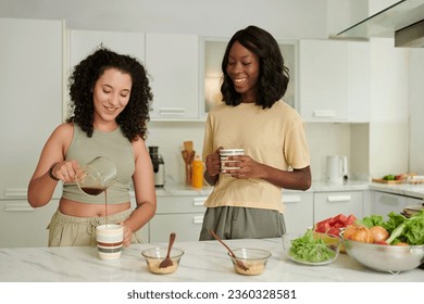 Happy woman pouring coffee in cup when standing next to roommate - Powered by Shutterstock