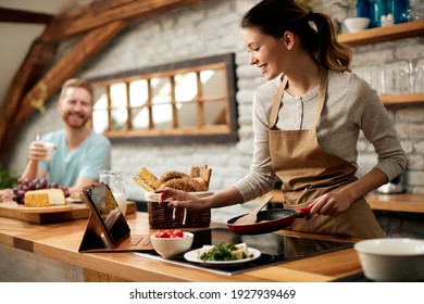 Happy woman preparing food while following recipe on digital tablet in the kitchen.  - Powered by Shutterstock