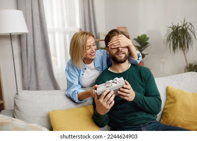 Happy Woman Presenting Gift To Husband. Excited Young Woman Closed Eyes Presenting Good Unexpected Present To Husband At Home. Loving Girlfriend Making Romantic Surprise To Boyfriend  - Powered by Shutterstock