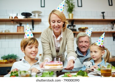 Happy Woman Putting Birthday Cake On Festive Table For Her Family