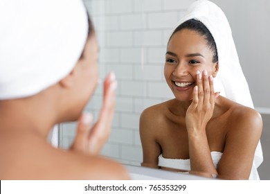 Happy Woman Putting On Facial Moisturizer With Hand In Bathroom Mirror