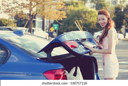 Happy woman putting shopping bags inside car trunk