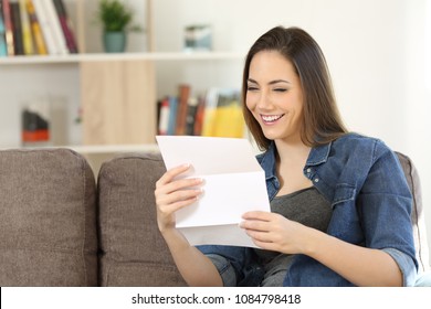 Happy woman reading a letter sitting on a couch in the living room at home