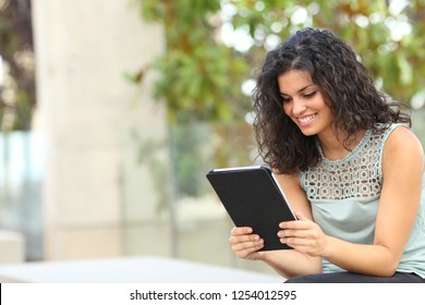 Happy Woman Reading Online Content In A Tablet Or Ebook Sitting On A Bench In A Park