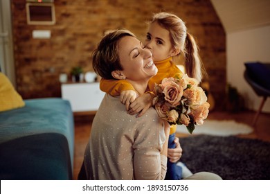 Happy Woman Receiving Bouquet Of Flowers From Her Daughter Who Is Kissing Her At Home.