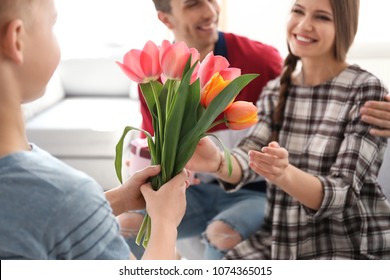 Happy Woman Receiving Flowers And Gift From Her Family At Home. Mother's Day Celebration