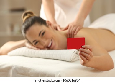 Happy Woman Receiving A Massage Showing Blank Credit Or Gift Card In A Spa Salon