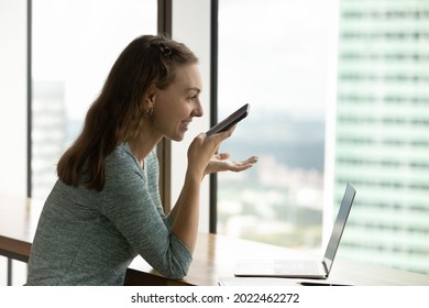 Happy Woman Recording Audio Message On Smartphone, Having Telephone Call On Speaker, Using Voice Recognition App. Gen Z Girl Giving Command To Virtual Assistant On Mobile Phone At Laptop