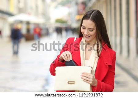 Happy woman in red taking out the phone from the bag in the street in winter
