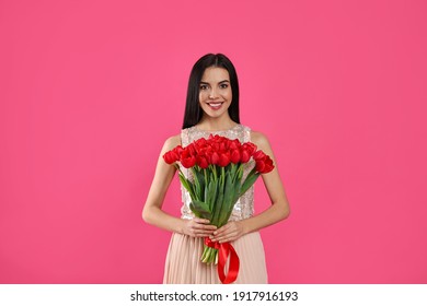 Happy woman with red tulip bouquet on pink background. 8th of March celebration