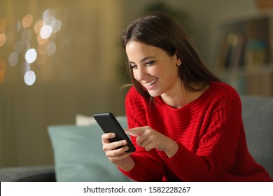 Happy Woman In Red Using Mobile Phone Sitting On A Couch In The Night At Home