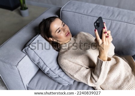 Happy woman relax on comfortable couch at home texting messaging on smartphone, smiling girl use cellphone, browse wireless internet on gadget, shopping online from home