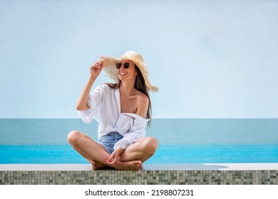 Happy woman relaxing by a swimming pool. Attractive female wearing straw hat and sunglasses while looking away and smiling.  - Powered by Shutterstock