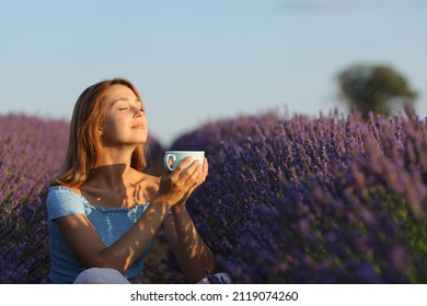 Happy woman relaxing drinking coffee in lavender field at sunset