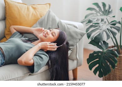 Happy Woman Relaxing In Her Sofa At Home, Smiling Girl Is Listening To Music With Headphones And Lying Down With Eyes Closed, Enjoy Good Quality Sound, Stress Free Concept.