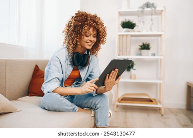 Happy Woman Relaxing at Home, Smiling and Chatting with Friends Online Using Tablet PC and Headphones on Cozy Couch - Powered by Shutterstock