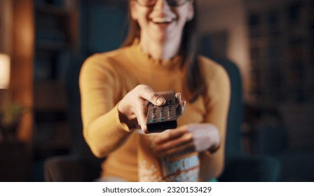 Happy woman relaxing at home and watching movies on TV, she is holding the remote control - Shutterstock ID 2320153429