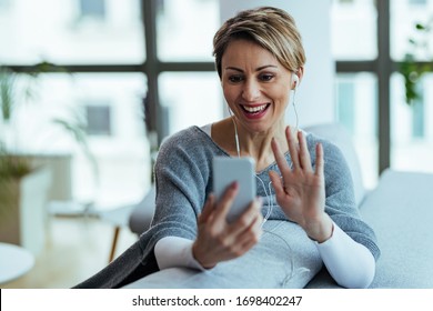 Happy woman relaxing at home and waving while having video call over mobile phone.