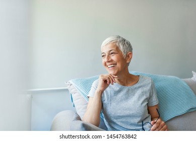 Happy woman relaxing on her couch at home in the sitting room. Portrait of beautiful mature woman smiling while sitting at sofa at home. Beautiful middle age woman smiling at home - Powered by Shutterstock