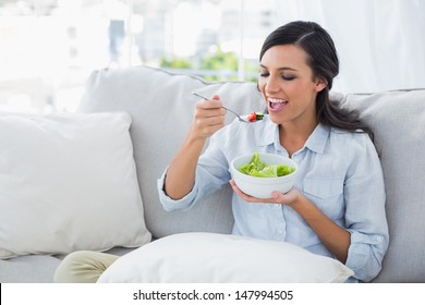 Happy Woman Relaxing On The Sofa Eating Salad In Her Living Room