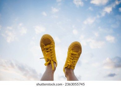 Una mujer feliz descansa y empuja sus zapatillas al cielo para disfrutar de la vista. Pies femeninos por delante del cielo nublado