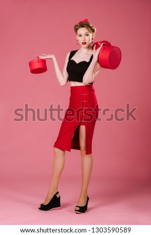 Happy woman in retro style holding red shopping bags on the pink background. Pinup portrait